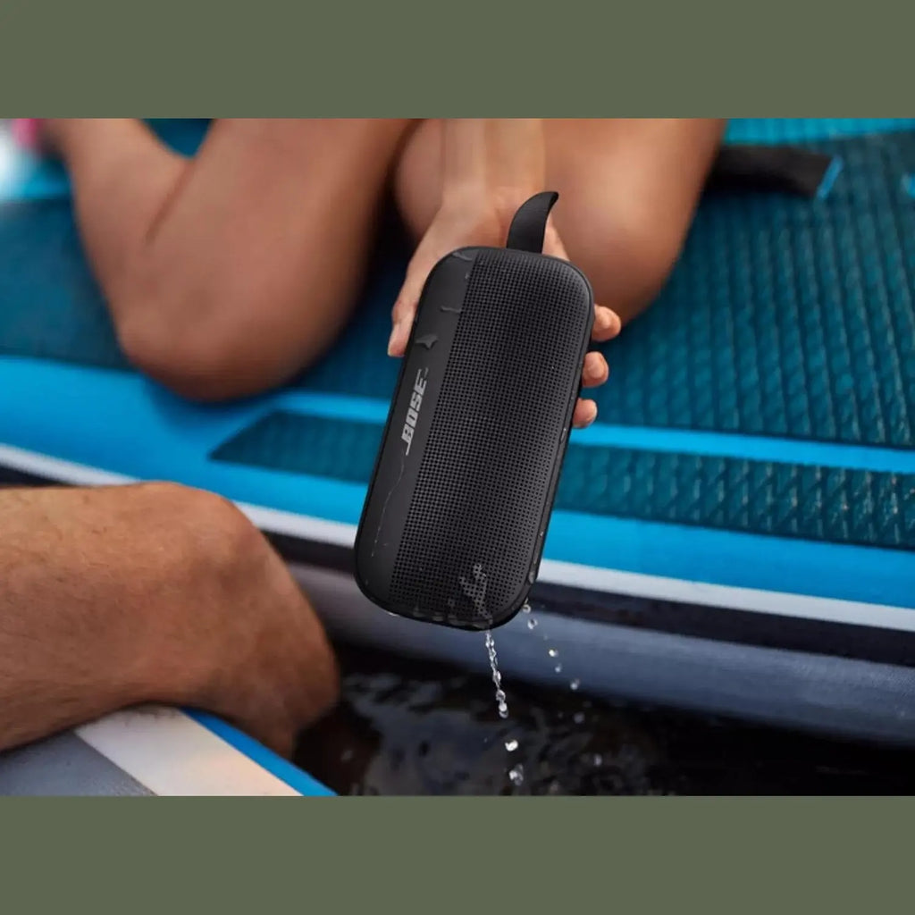 Black Bose SoundLink Flex speaker held over water demonstrating waterproof use