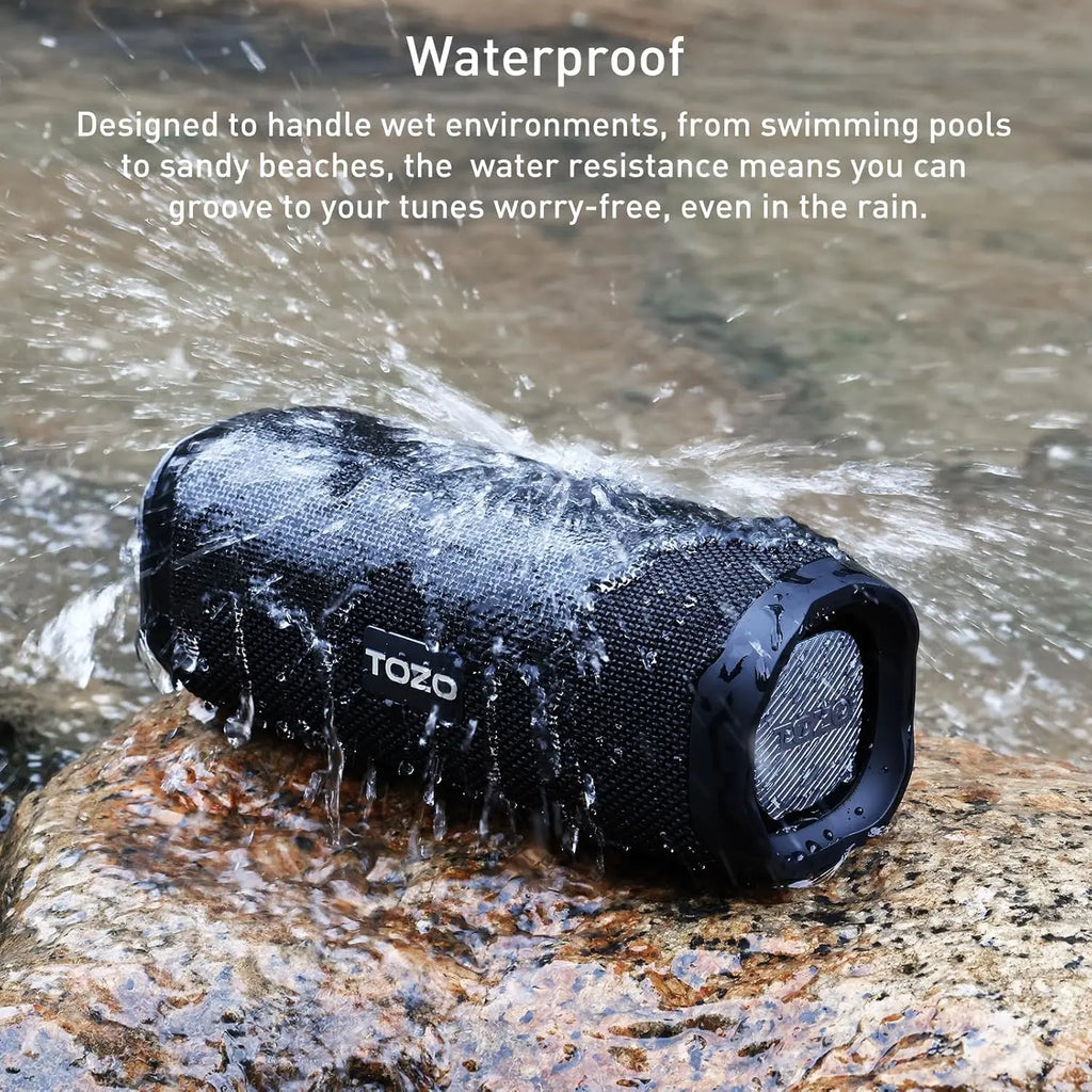 Waterproof black TOZO PA2 speaker splashing in water on rock surface