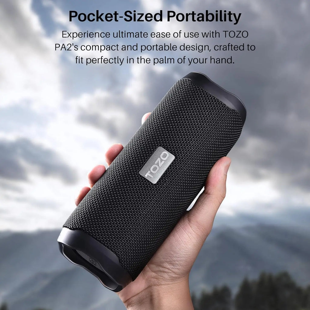 Compact black TOZO PA2 speaker held in hand against mountain backdrop